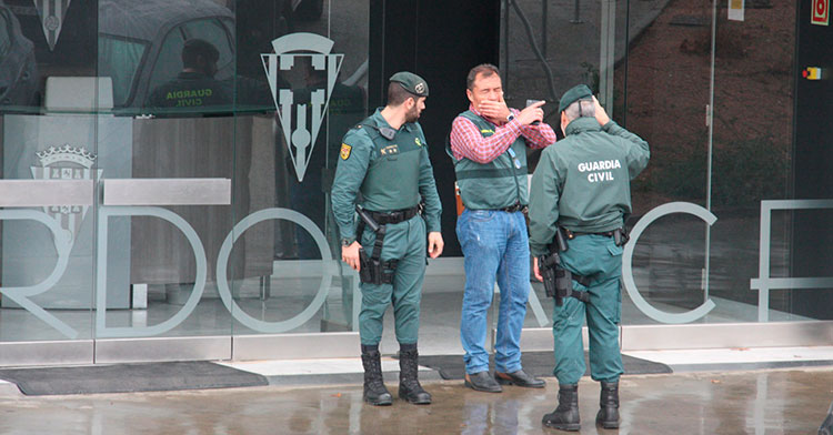 Un policía judicial dando instrucciones a dos guardias civiles en la puerta de acceso a las oficinas de El Arcángel