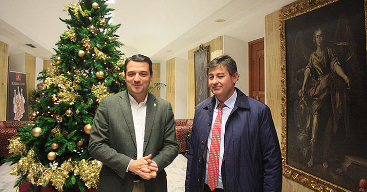 El alcalde José María Bellido posando junto a Javier González con el árbol de Navidad al fondo y San Rafael presente en el cuadro de la derecha