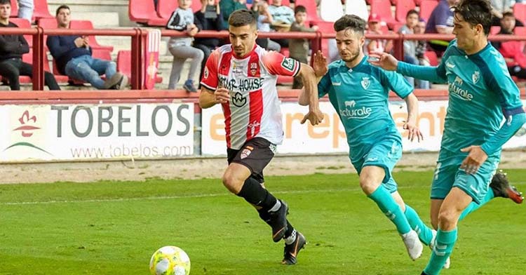 Zelu conduciendo el balón por delante de dos jugadores del filial de Osasuna.