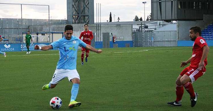 Un jugador del Ciudad de Lucena desplaza el balón en largo ante la llegada de un contrario del Utrera.