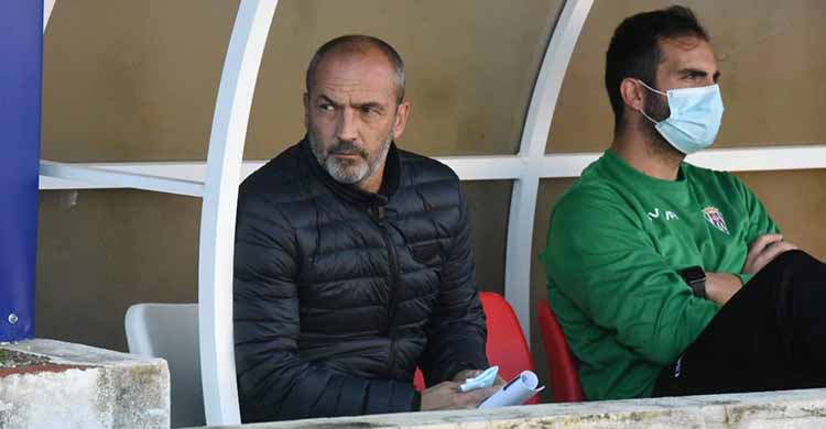 Sabas, con cara de pocos amigos, sentando en el banquillo de Linarejos junto a Rubén, su preparador físico.