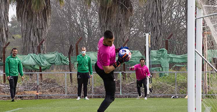 Edu Frías tras atrapar un balón aéreo, con Miguel de las Cuevas al fondo trabajando la recuperación con Javi Poveda.