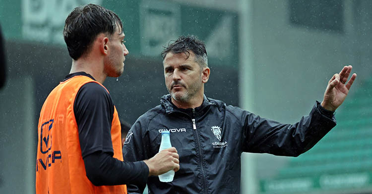 Álex Sala escuchando a Iván Ania bajo la lluvia.