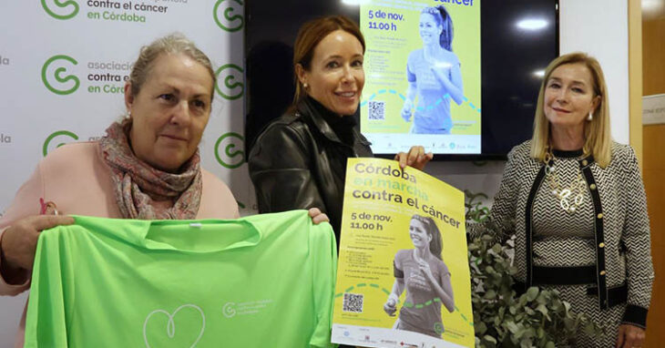 La presidenta del IMDECO, Marian Aguilar, mostrando el cartel y la camiseta de la prueba junto a dos representantes de la Asociación Española contra el cáncer.