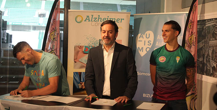 Antonio Fernández Monterrubio presentando el acuerdo de colaboración con las tres Asociaciones con Álex Sala luciendo una de las camisetas benéficas y Jesús Aguilar, representando a la Asociación Saca la Lengua a la ELA firmando el acuerdo.
