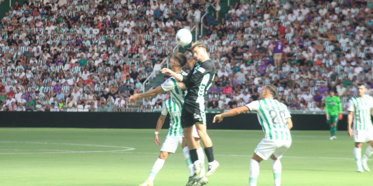 Pedro Ortiz y Jacobo pelean por un balón dividido con un bético enfocados por una luz desconcertante con sombras de fondo.