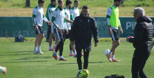 Pensativo, Iván Ania con el balón en los pies y sus pupilos al fondo.